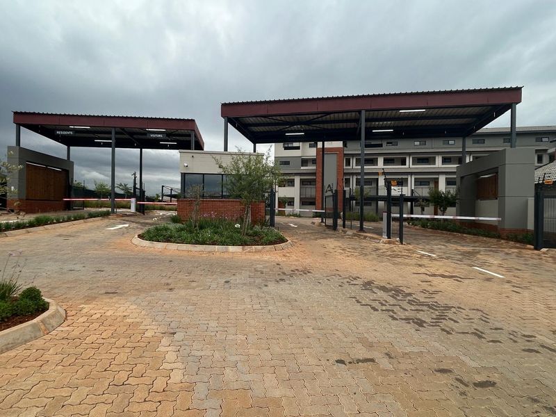Modern apartment complex entrance featuring a secure gatehouse, boom gate access control, and paved driveway infrastructure.
