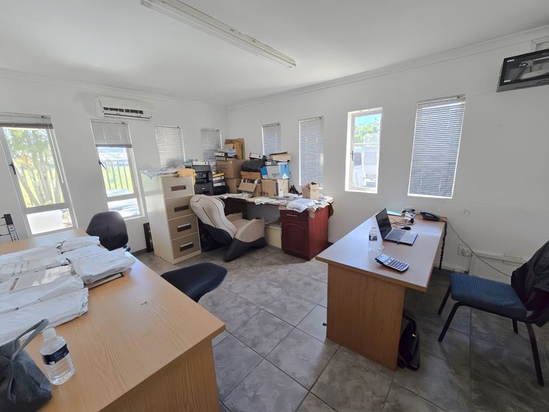 A functional office space featuring tiled flooring, multiple windows with venetian blinds, and a wall-mounted air conditioning unit.