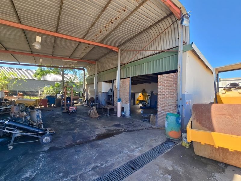 Industrial workshop area featuring a large covered workspace with concrete flooring, steel structural framing, and open access for heavy machinery or vehicle maintenance.