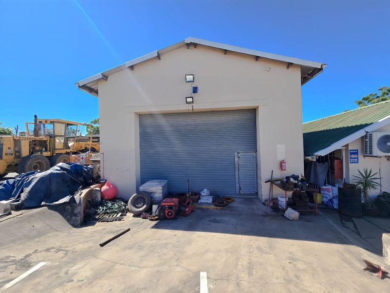 Industrial warehouse exterior featuring a large roller shutter door, security access door, and external floodlighting on a concrete apron.