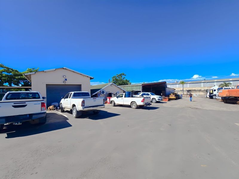 Industrial property exterior featuring a large asphalt yard, multiple warehouse structures with roller shutter doors, and ample space for vehicle access and parking.