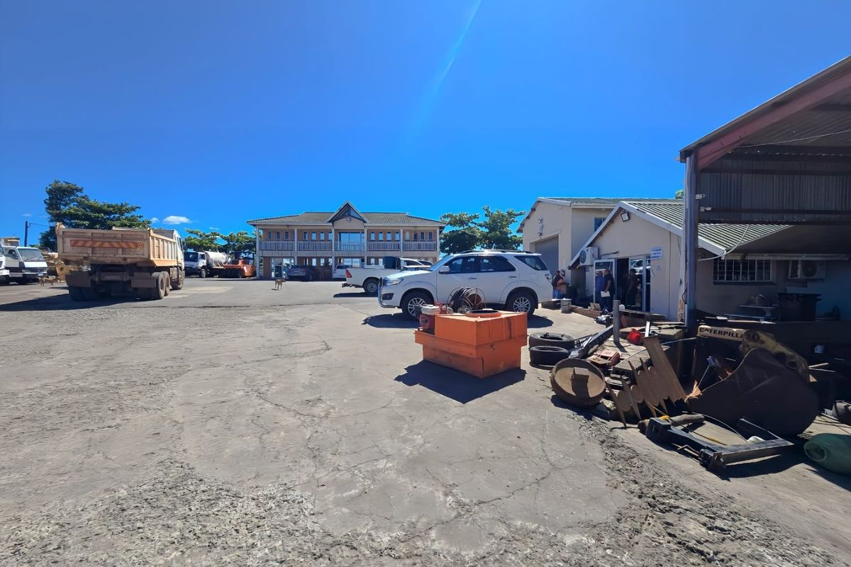 Industrial property yard featuring a multi-story office building, warehouse structure with covered loading area, and paved parking space.