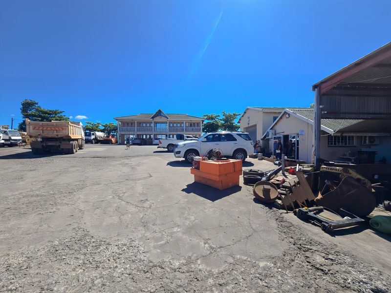 Industrial property yard featuring a multi-story office building, warehouse structure with covered loading area, and paved parking space.