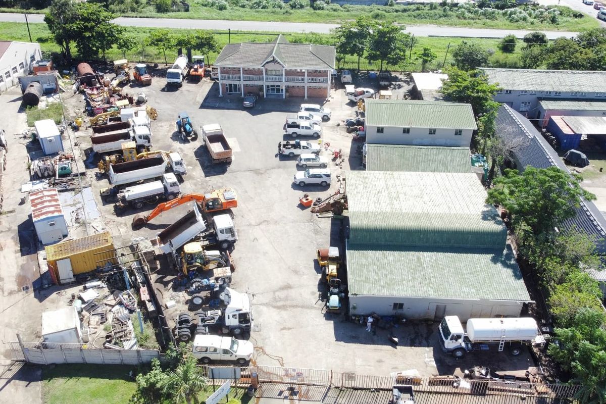 Aerial view of an industrial property featuring multiple warehouse structures, an office building, and a large paved yard area for vehicle and equipment storage.