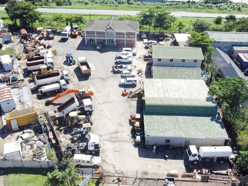 Aerial view of an industrial property featuring multiple warehouse structures, an office building, and a large paved yard area for vehicle and equipment storage.
