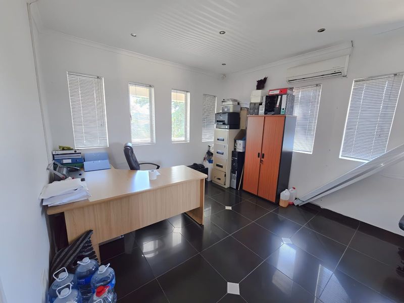 A functional office space featuring tiled flooring, recessed downlighting, split-system air conditioning, and multiple windows with fitted venetian blinds.