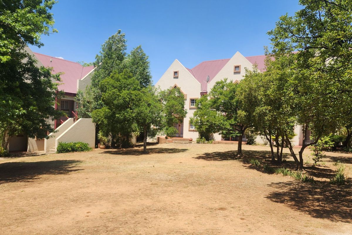 A view of the apartment complex exterior featuring a shared garden area, mature trees, and traditional pitched roof architecture.