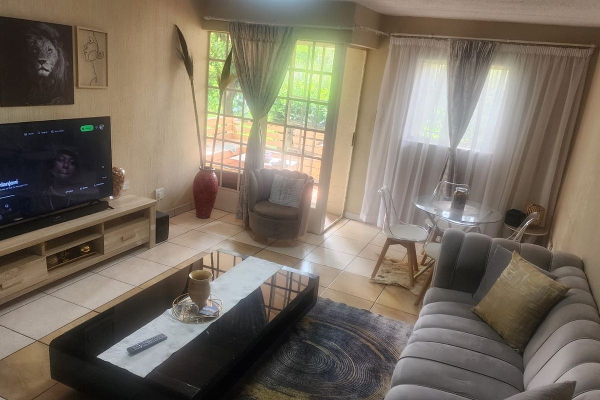 A comfortable living room featuring tiled flooring, natural light from a large window, and direct access to an outdoor patio area.
