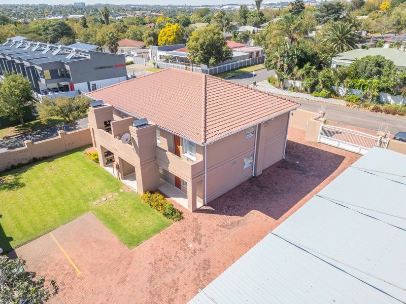 Aerial view of a multi-story apartment building featuring a tiled roof, paved driveway, perimeter wall, and private balconies.