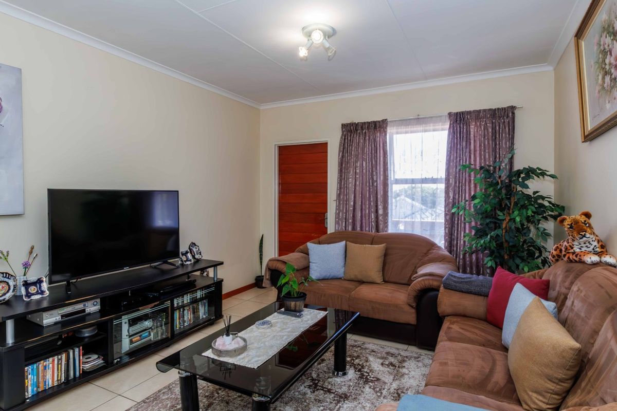 A comfortable living room featuring tiled flooring, neutral wall finishes, and a timber door, providing a functional and well-lit space for relaxation.