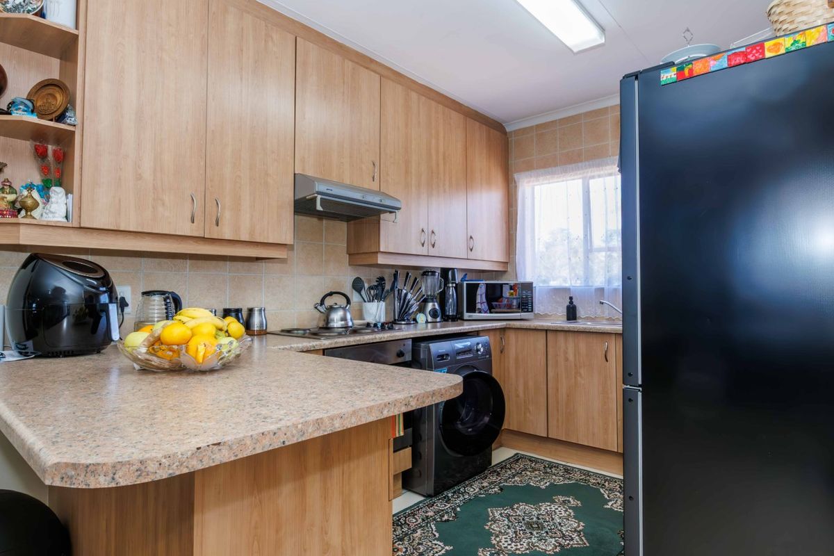 A functional kitchen featuring light wood-finish cabinetry, laminate countertops, tiled backsplash, and integrated appliances, offering a practical layout for daily use.