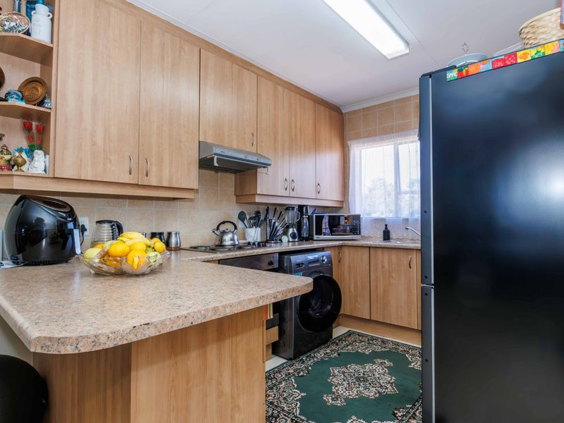 A functional kitchen featuring light wood-finish cabinetry, laminate countertops, tiled backsplash, and integrated appliances, offering a practical layout for daily use.