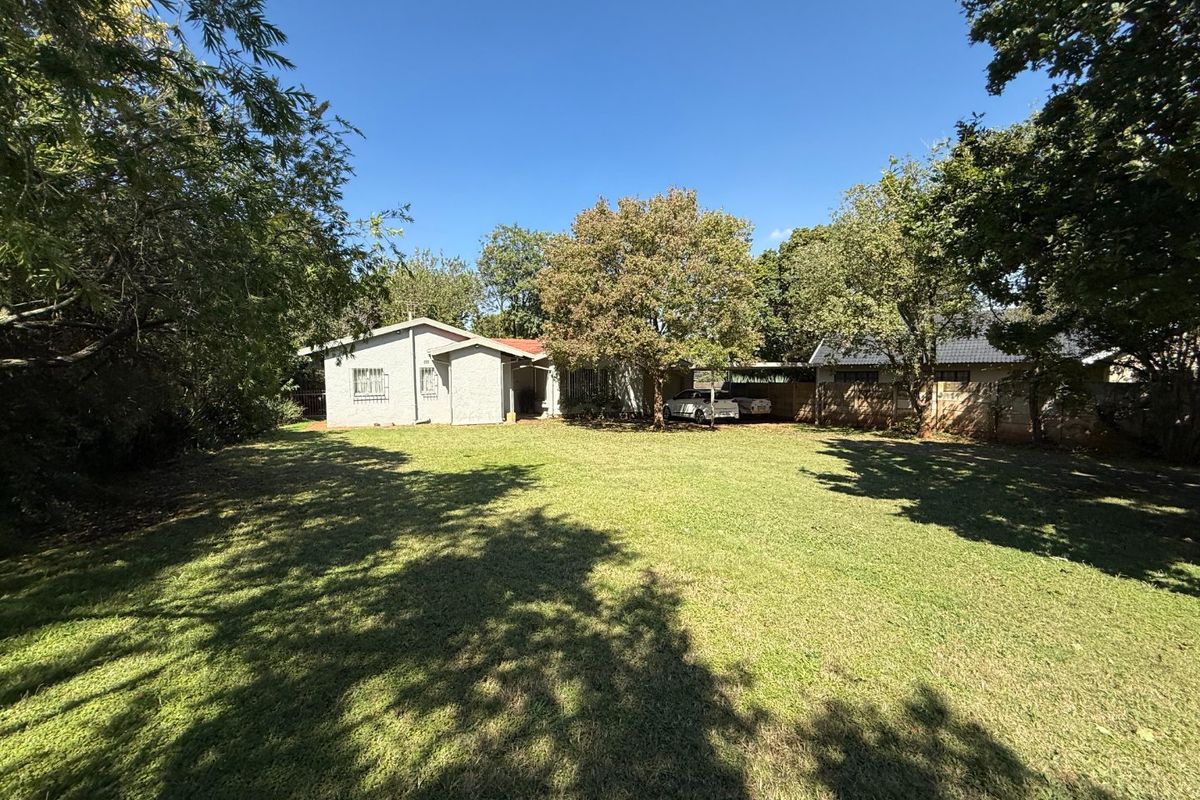 A spacious rear garden featuring a large lawn, mature trees, and a functional carport area attached to the main dwelling.