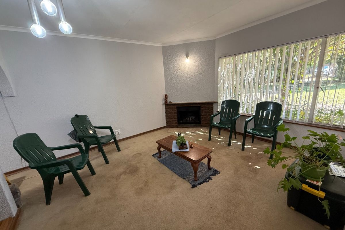 Living room featuring a brick fireplace, large windows with vertical blinds, and neutral wall finishes, offering a functional space for relaxation.