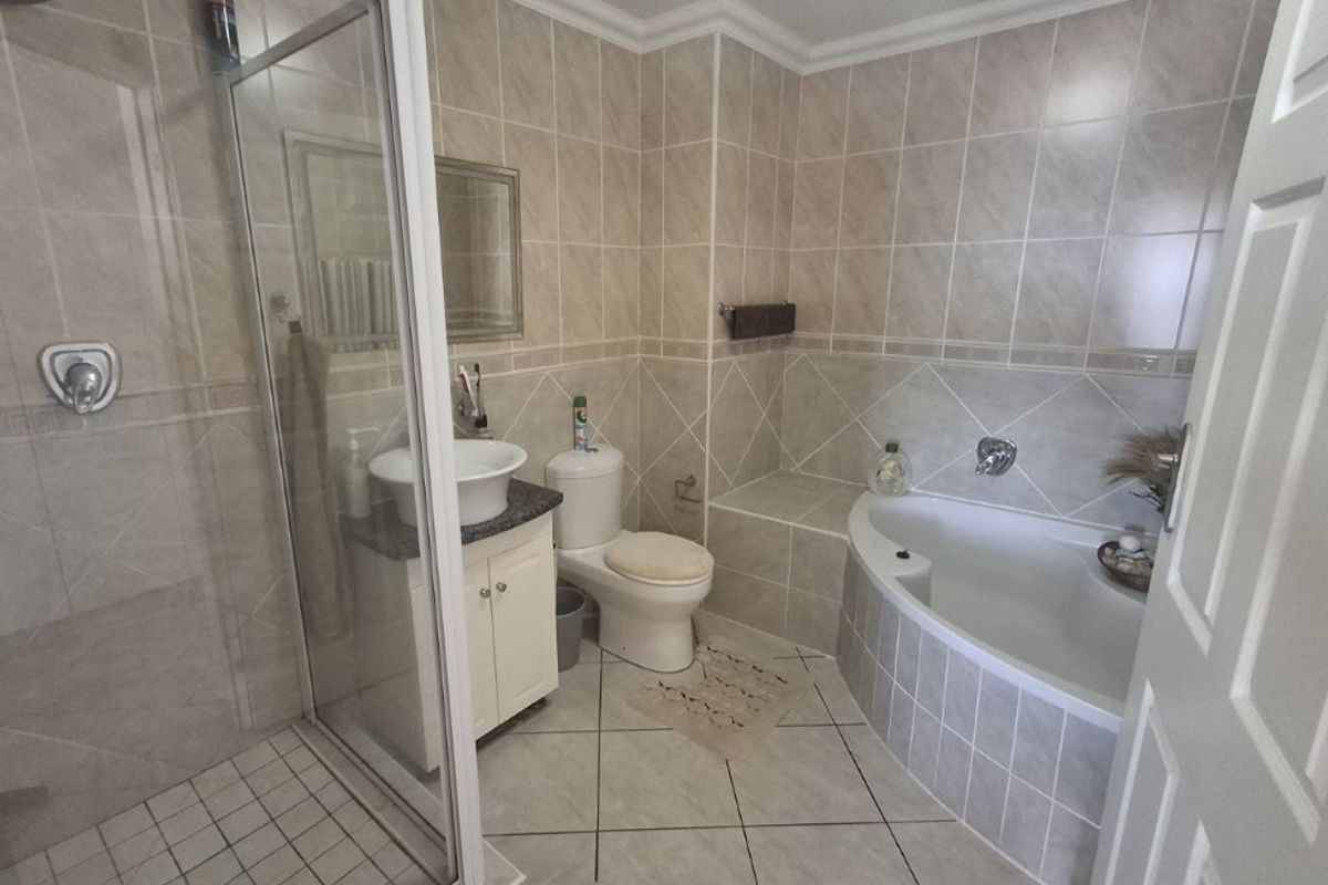 A functional bathroom featuring a glass-enclosed shower, a built-in bathtub, a vanity with a vessel sink, and neutral ceramic wall and floor tiling.