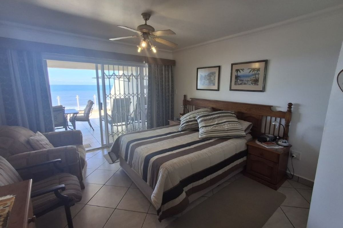 Spacious bedroom featuring tiled flooring, a ceiling fan, and sliding glass doors that open onto a balcony with ocean views.