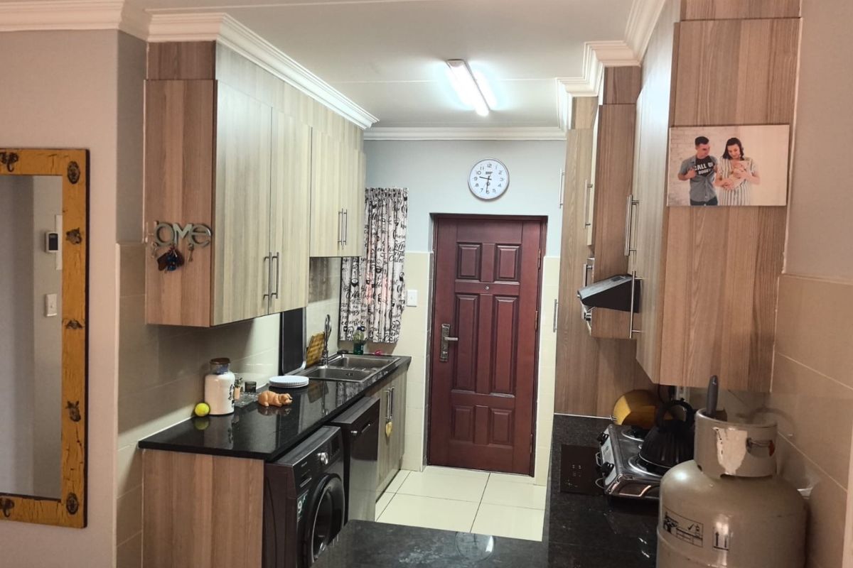 A functional kitchen featuring wood-look laminate cabinetry, dark granite countertops, integrated hob, and tiled flooring with direct access to an exterior door.