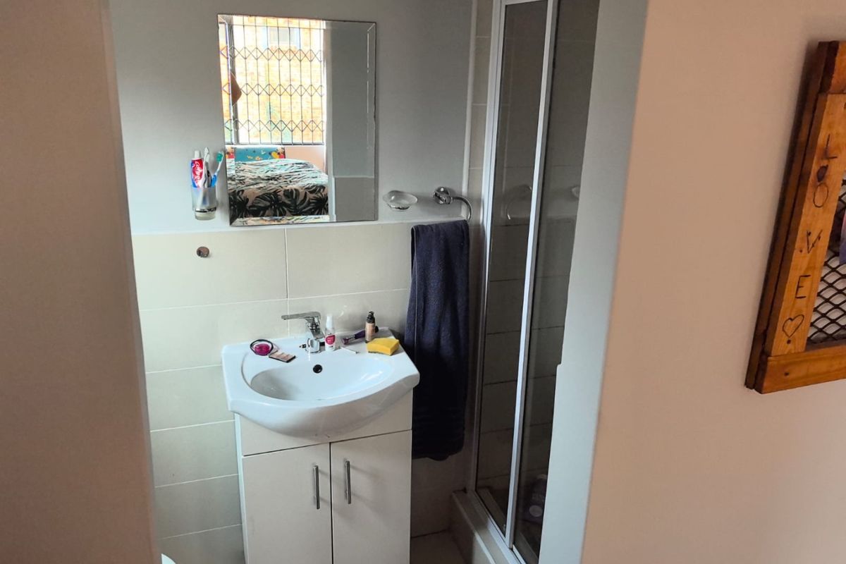 A compact bathroom featuring a vanity cabinet with a basin, a shower enclosure, and a wall-mounted mirror.