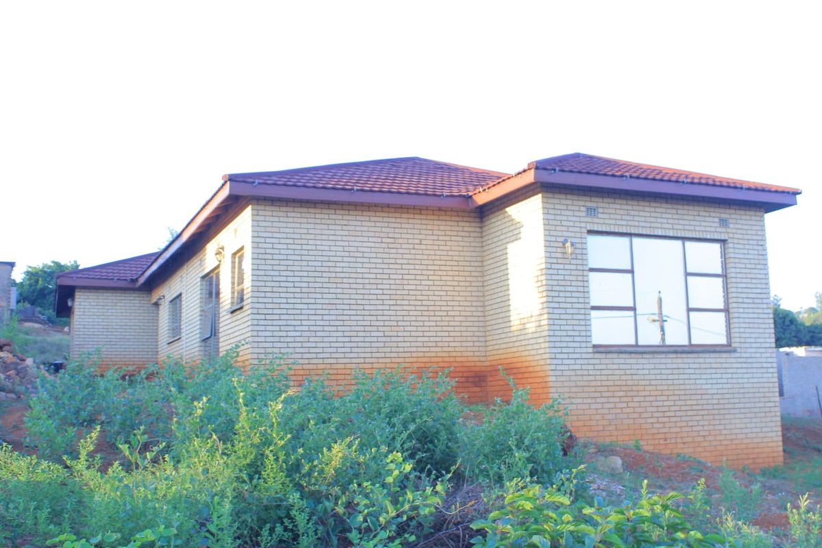 Rear view of a single-story brick house with a tiled roof, featuring aluminium window frames and visible exterior wall staining.