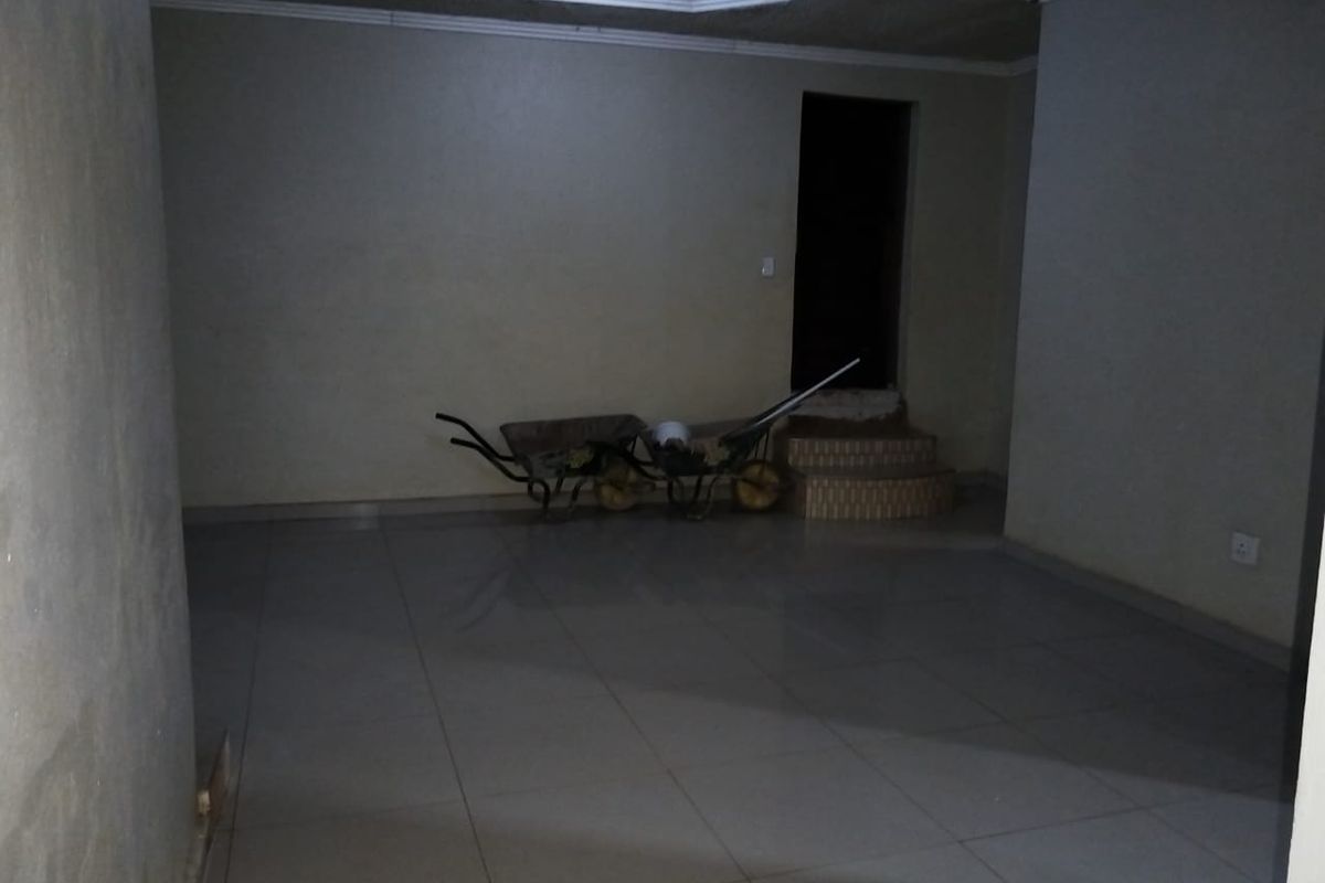 An empty, dimly lit living area featuring tiled flooring, coved ceiling details, and a small raised platform leading to an adjacent space.