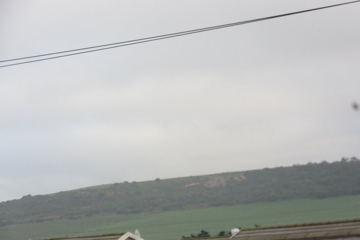A distant view of a grassy hillside and landscape under an overcast sky, captured from an elevated position.