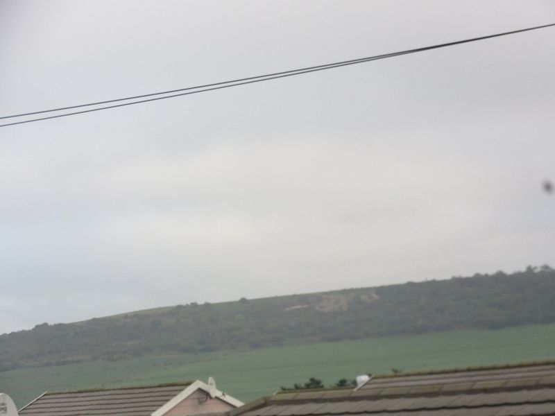 A distant view of a grassy hillside and landscape under an overcast sky, captured from an elevated position.