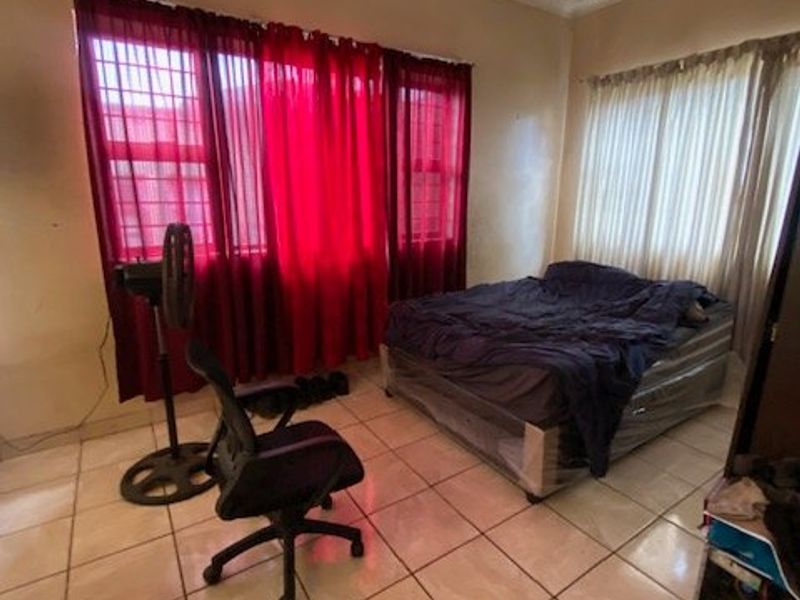 A bedroom featuring tiled flooring, ceiling detailing, and large windows with security bars, offering a functional space ready for cosmetic updates.