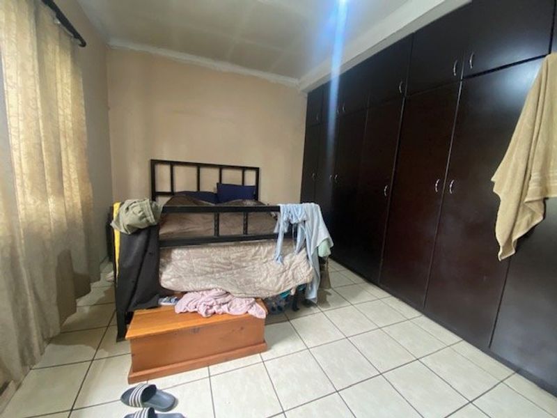 Bedroom featuring dark built-in cupboards and tiled flooring. The room requires cosmetic updates to the walls and ceiling to improve its overall condition.
