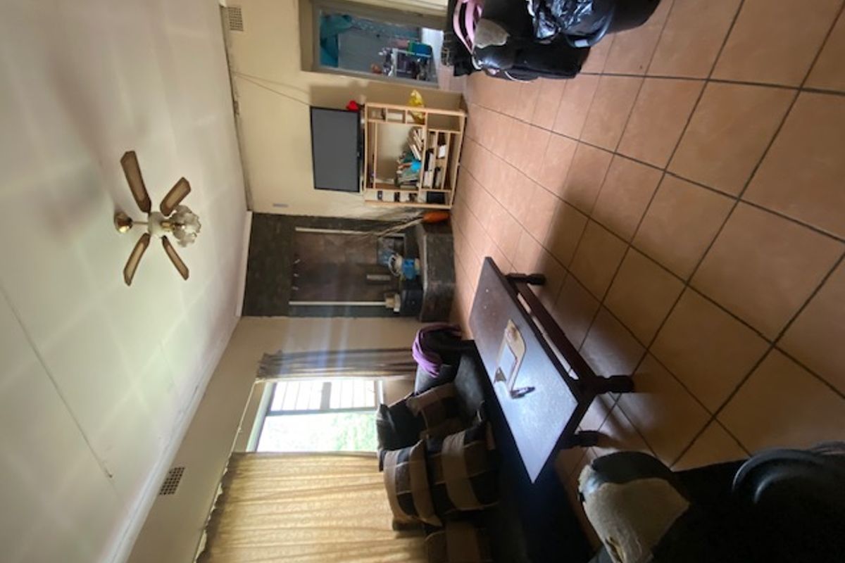 Living room featuring tiled flooring, a central ceiling fan, and a stone fireplace, requiring cosmetic updates to improve the overall aesthetic.