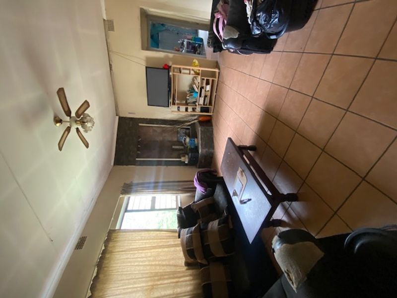 Living room featuring tiled flooring, a central ceiling fan, and a stone fireplace, requiring cosmetic updates to improve the overall aesthetic.