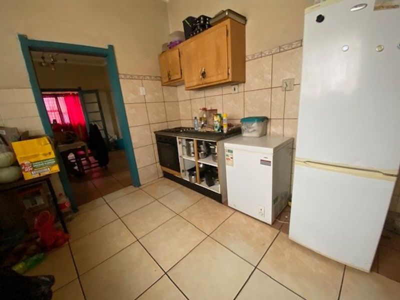 A dated kitchen featuring tiled walls and flooring, built-in cabinetry with an integrated oven and hob, requiring cosmetic updates to modernize the space.