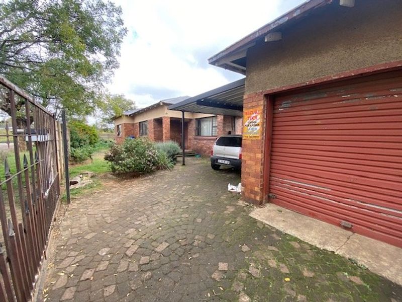 Front exterior view of the property featuring a brick driveway, attached garage with metal door, and a carport entrance.