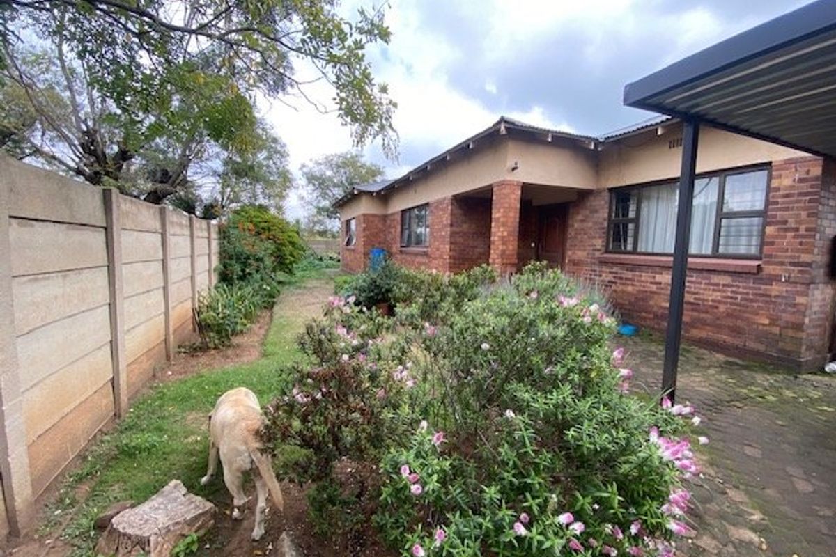 Rear view of a brick house featuring a paved patio area, precast boundary wall, and established garden space.