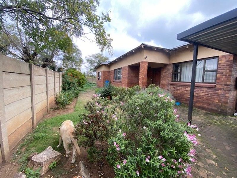 Rear view of a brick house featuring a paved patio area, precast boundary wall, and established garden space.