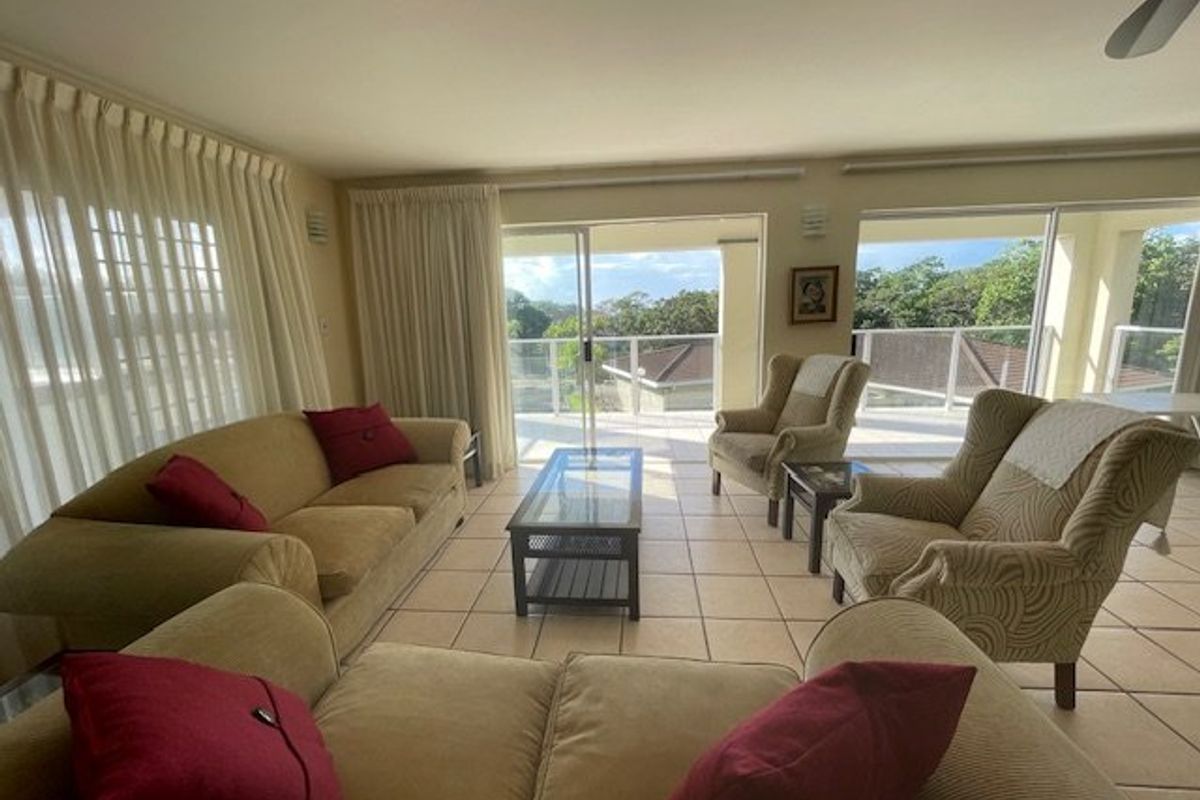 Spacious living room featuring tiled flooring, ceiling fan, and large sliding glass doors providing direct access to a balcony with scenic views.