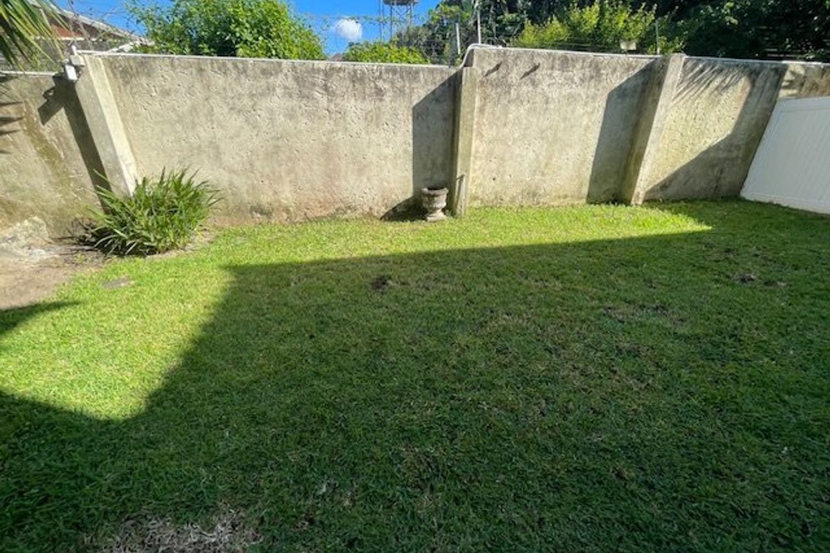 A private rear garden area featuring a lawn and a high concrete boundary wall.