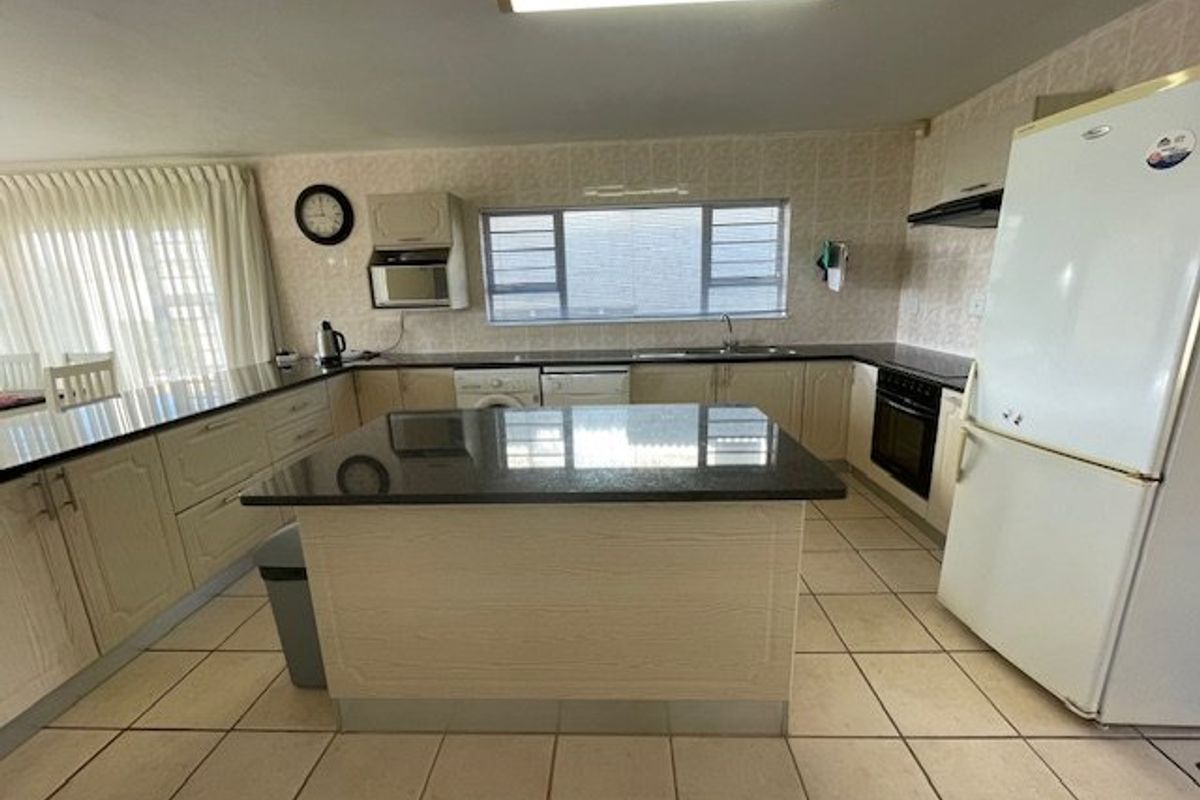 A functional kitchen featuring granite countertops, a central island, built-in oven, extractor fan, and tiled flooring with ample cabinetry for storage.
