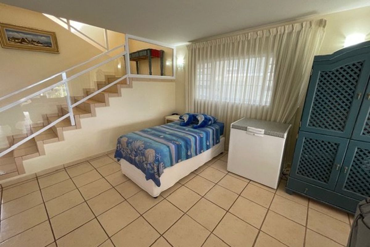 A bedroom featuring tiled flooring and an integrated staircase with a glass balustrade, offering a functional layout with natural light through curtained windows.