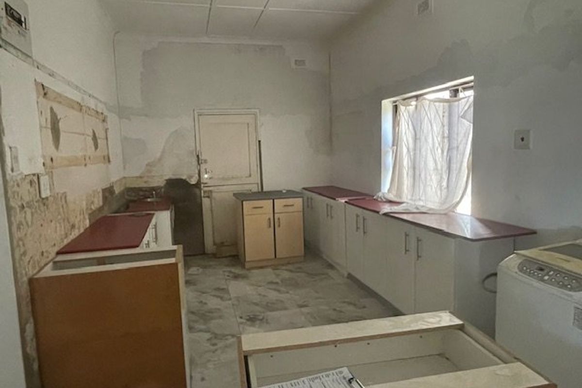 A kitchen space in need of renovation, featuring built-in cabinetry, tiled flooring, and significant wall surface damage requiring repair and repainting.