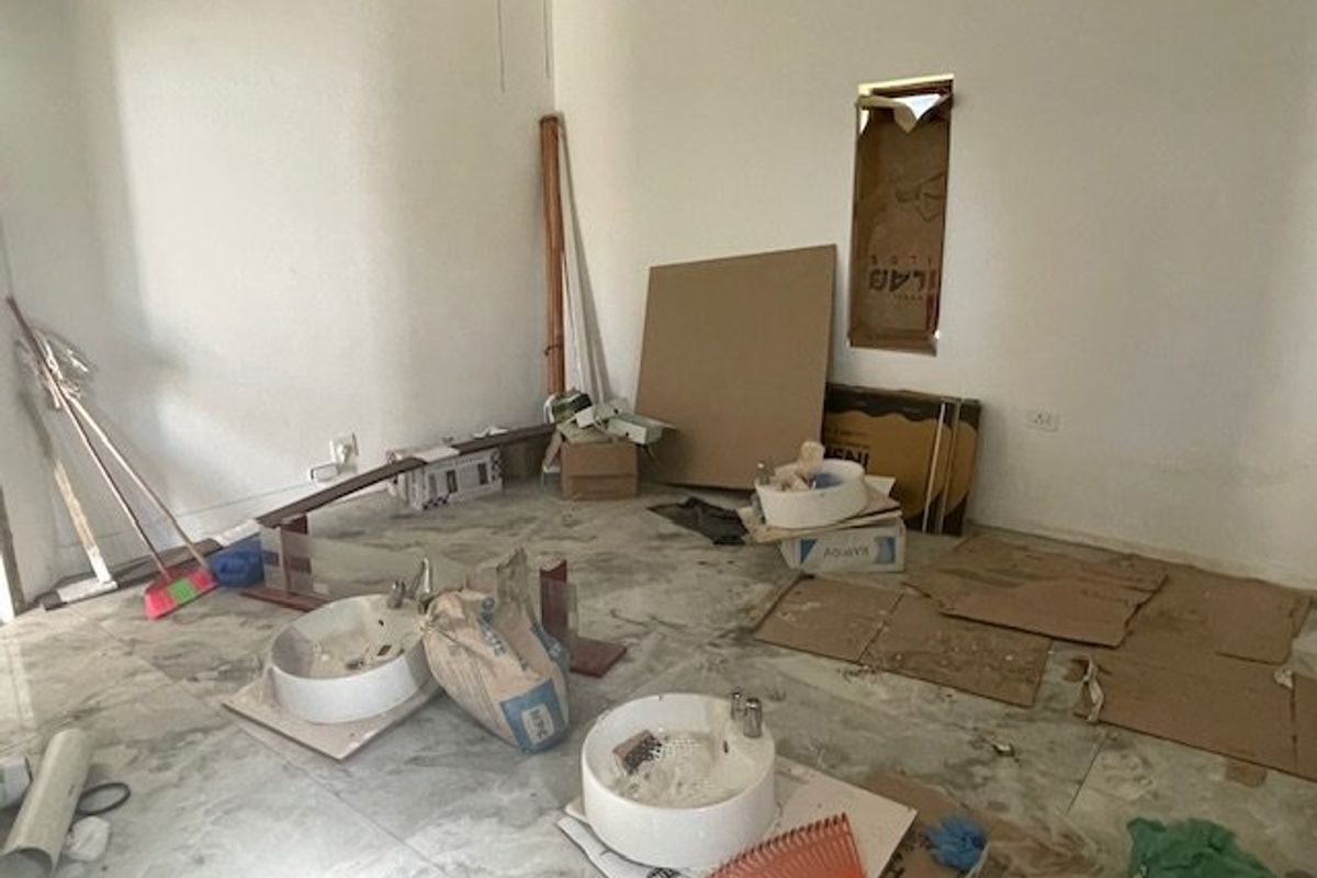 An unfinished bathroom space featuring tiled flooring and uninstalled vanity basins, currently undergoing renovation with exposed wall openings and construction materials present.