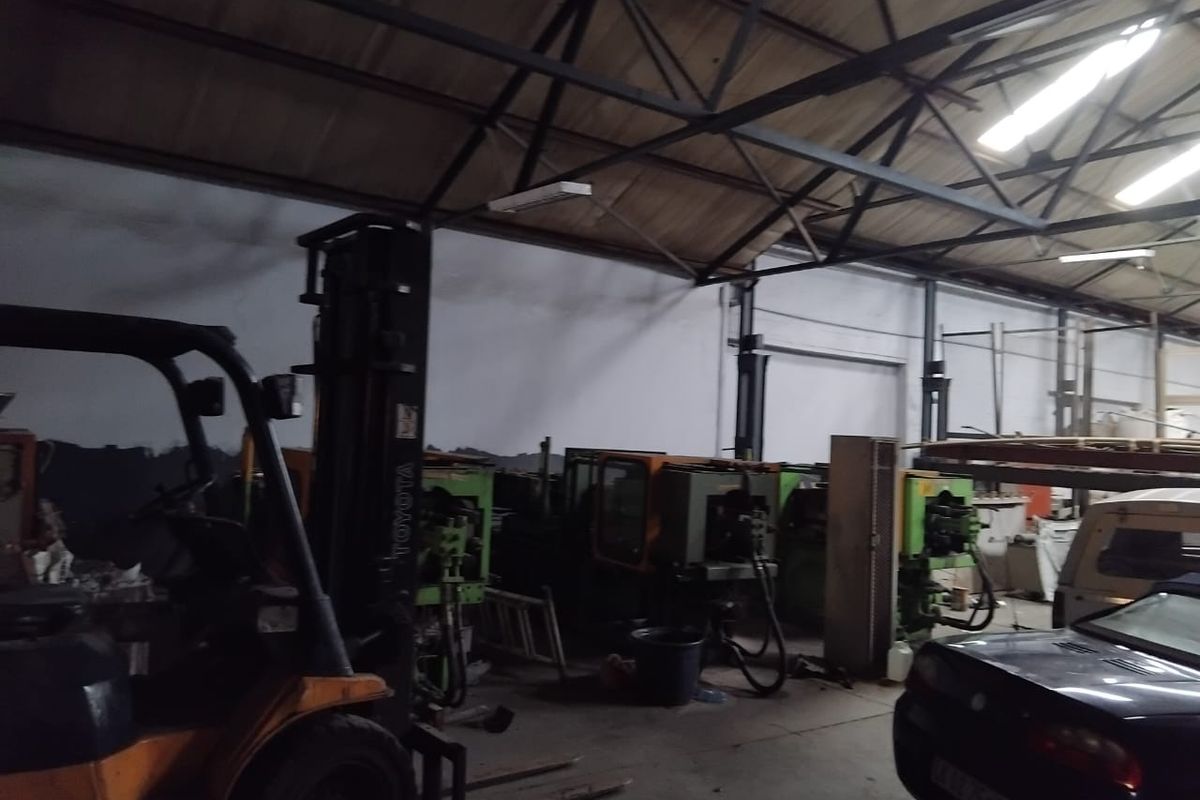 Industrial warehouse space featuring exposed steel roof trusses, concrete flooring, and functional overhead lighting, suitable for manufacturing or storage operations.