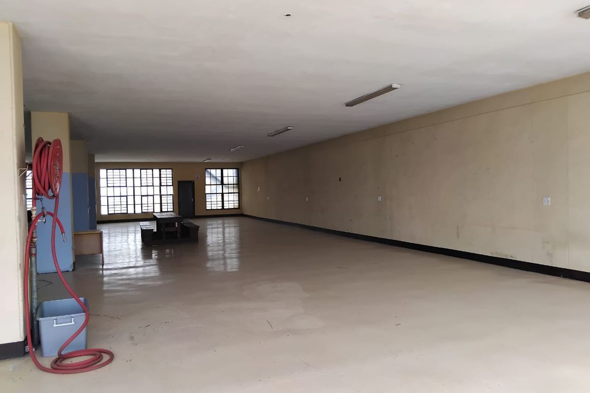 A large, open-plan commercial space featuring epoxy flooring, fluorescent lighting, and a wall-mounted fire hose reel, suitable for various business or office configurations.