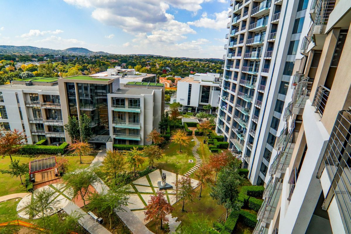 An elevated aerial view of a modern apartment complex featuring well-maintained landscaped gardens, paved pathways, and contemporary residential architecture.