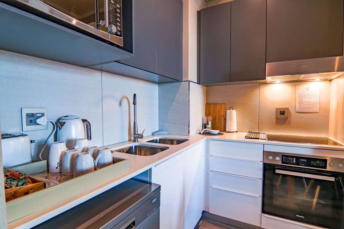Modern compact kitchen featuring sleek grey and white cabinetry, integrated appliances including an oven and hob, and high-quality stone countertops.