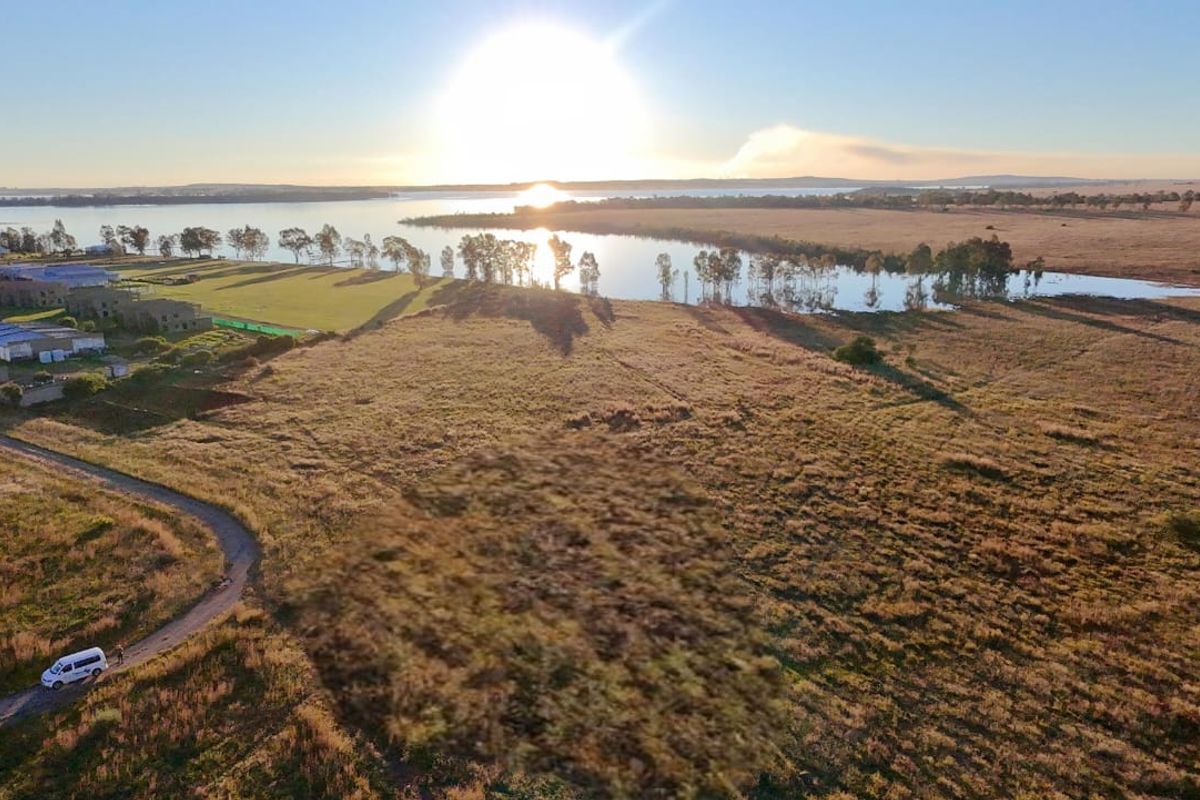 An aerial view of a large, vacant residential land parcel featuring expansive open fields and scenic water frontage.