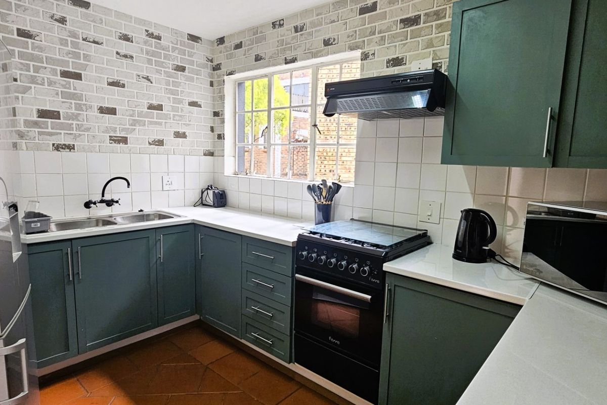 A functional kitchen featuring green cabinetry, a double basin sink, a freestanding stove with an extractor fan, and a brick-effect feature wall.
