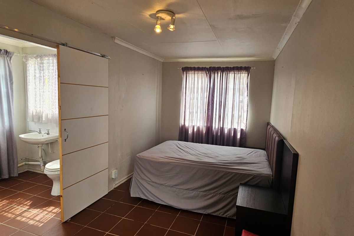A bedroom featuring tiled flooring and an en-suite bathroom with a sliding door, showing signs of wear on the ceiling and walls.