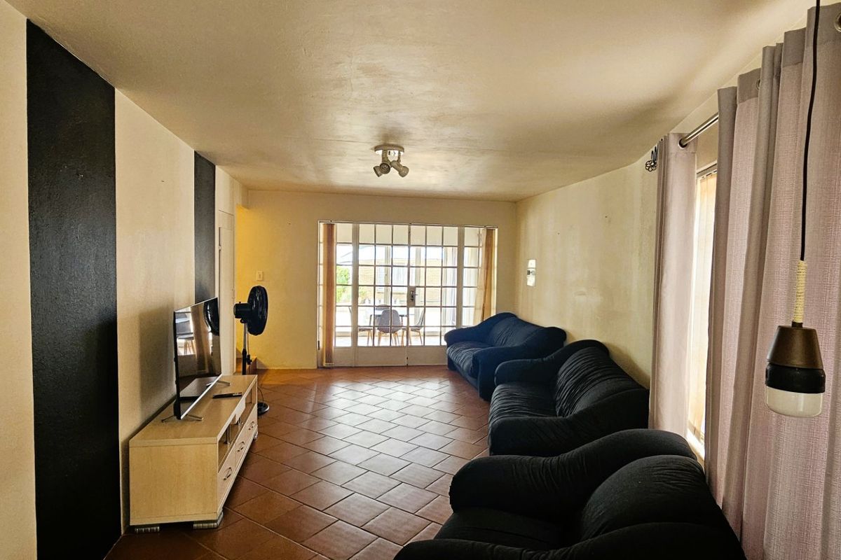 A living room featuring terracotta floor tiles and a sliding glass door leading to an outdoor area, providing natural light to the space.