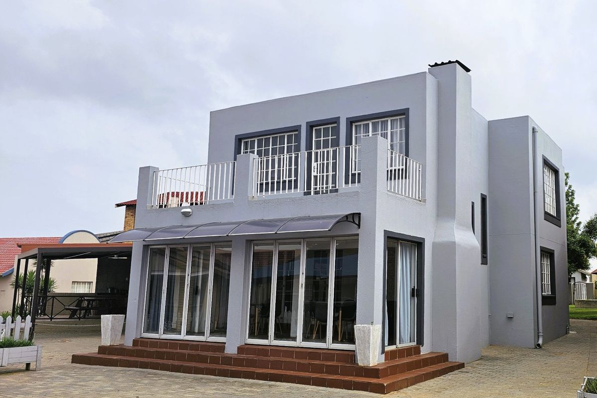 Rear view of a modern two-story apartment building featuring a balcony, large folding glass doors, and a paved outdoor area.