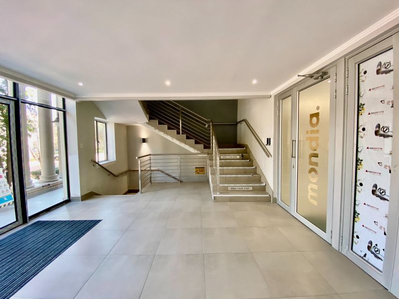 Modern commercial building entrance lobby featuring tiled flooring, stainless steel handrails, and a central staircase leading to upper and lower levels.